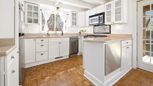 A modern kitchen with white cabinetry, a central island, and a microwave. - Cottage on Rush - Heart of Fayetteville (Fayetteville)