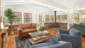 A spacious living room with a fireplace, large windows, and a high ceiling. - Cottage on Rush - Heart of Fayetteville (Fayetteville)