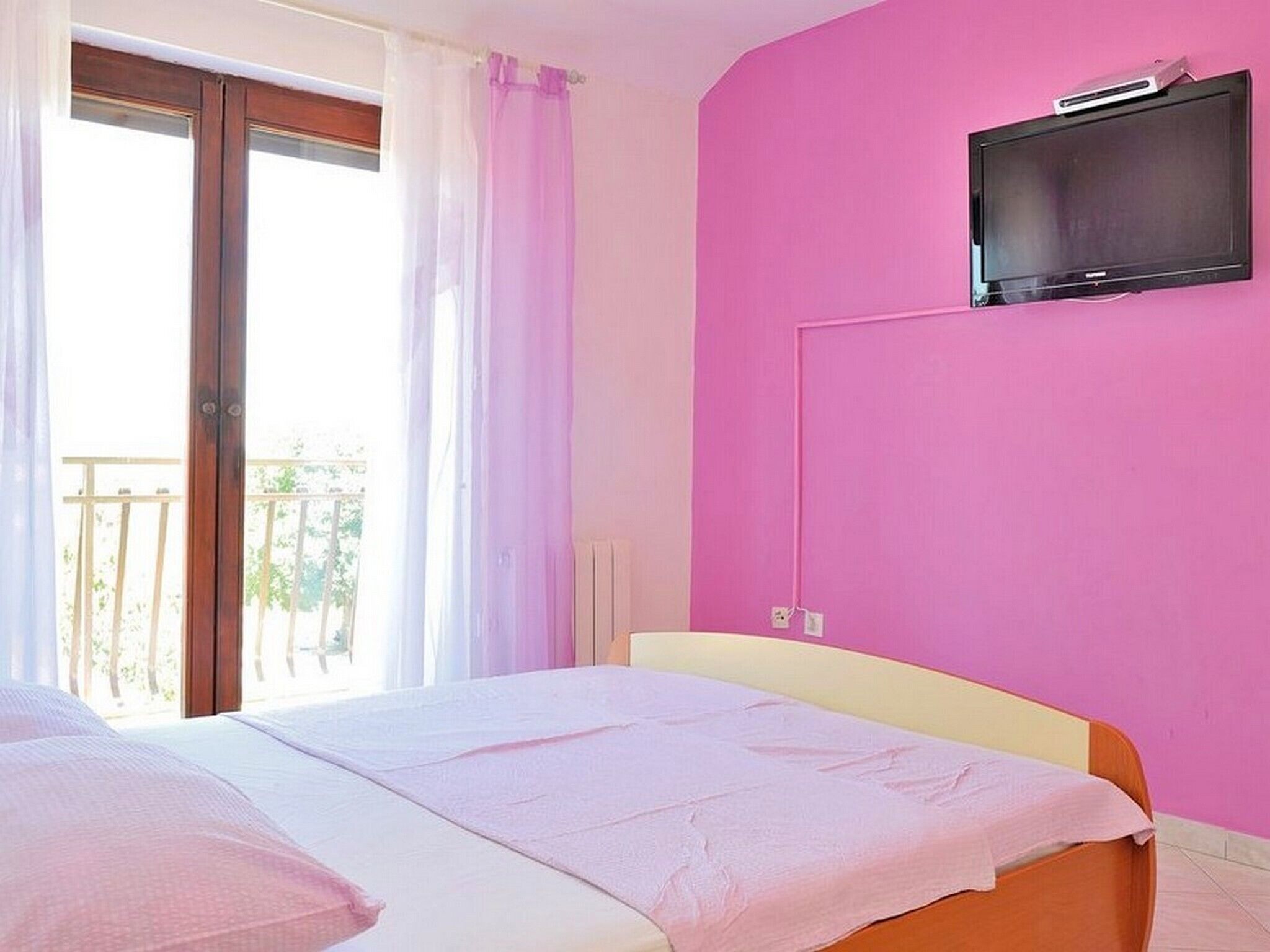 A bedroom with a bed, a television mounted on the wall, and a balcony with a view.