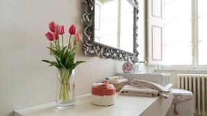 A bathroom with a white vanity, a vase of pink tulips, a crocheted item, and a mirror with an ornate frame.