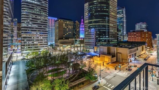 A cityscape at night with illuminated buildings, including a prominent 'Xactly' sign on a skyscraper.