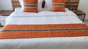 Un lit bien fait, avec du linge de lit blanc et deux coussins orange ornés d’un motif géométrique.
