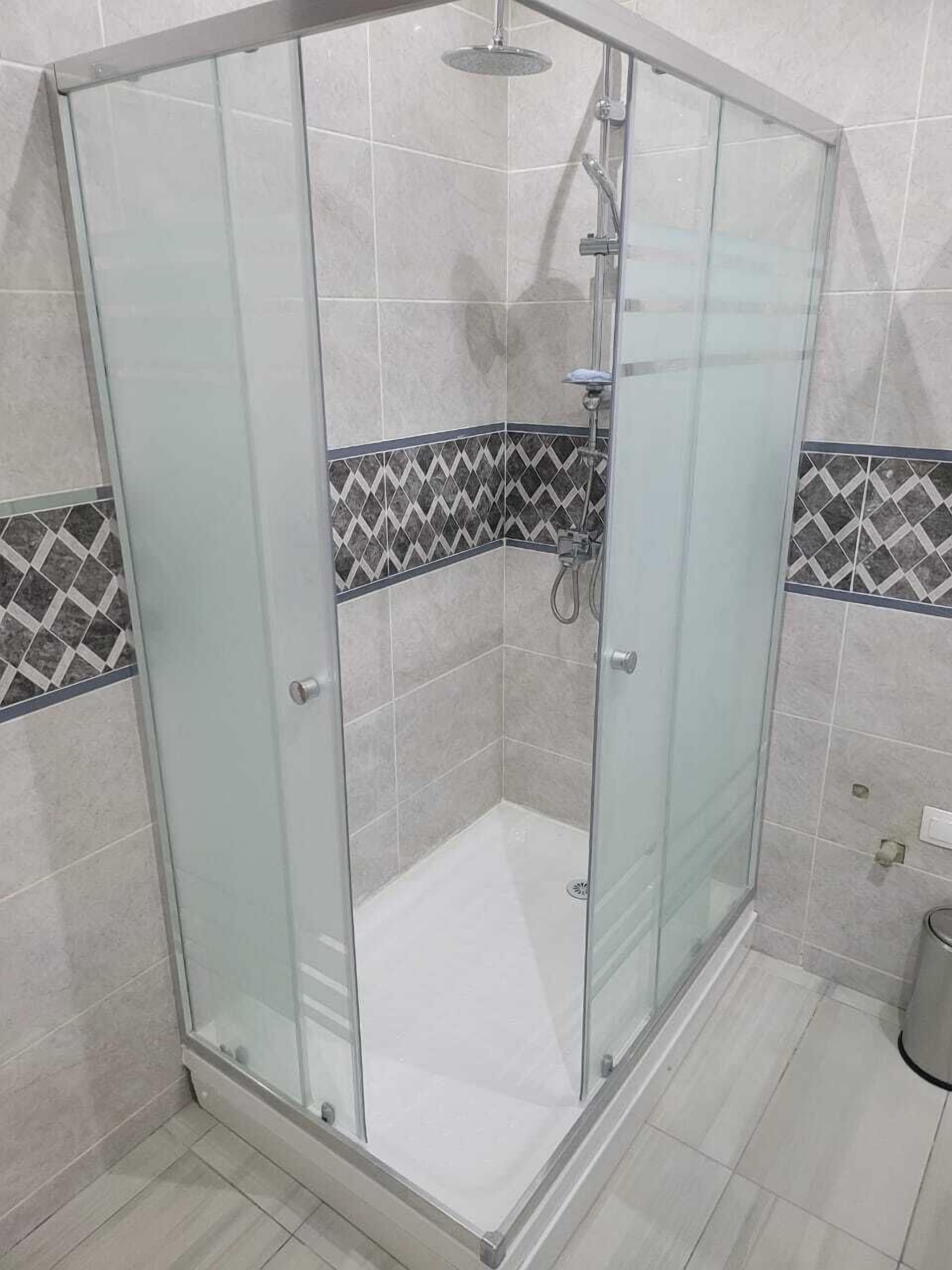 Eine Duschkabine mit Glaswänden, einer Duschbrause und Bedienfeld, geflieste Wände und ein Eckdesign.
