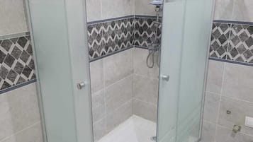 Eine Duschkabine mit Glaswänden, einer Duschbrause und Bedienfeld, geflieste Wände und ein Eckdesign.