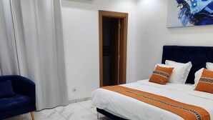 A modern bedroom with a bed, a blue chair, a fluffy rug, and a painting on the wall. - MARINA APPART HÔTEL  (Dakar)