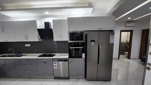 A modern kitchen with grey cabinets, stainless steel appliances, and a marble floor. - MARINA APPART HÔTEL  (Dakar)