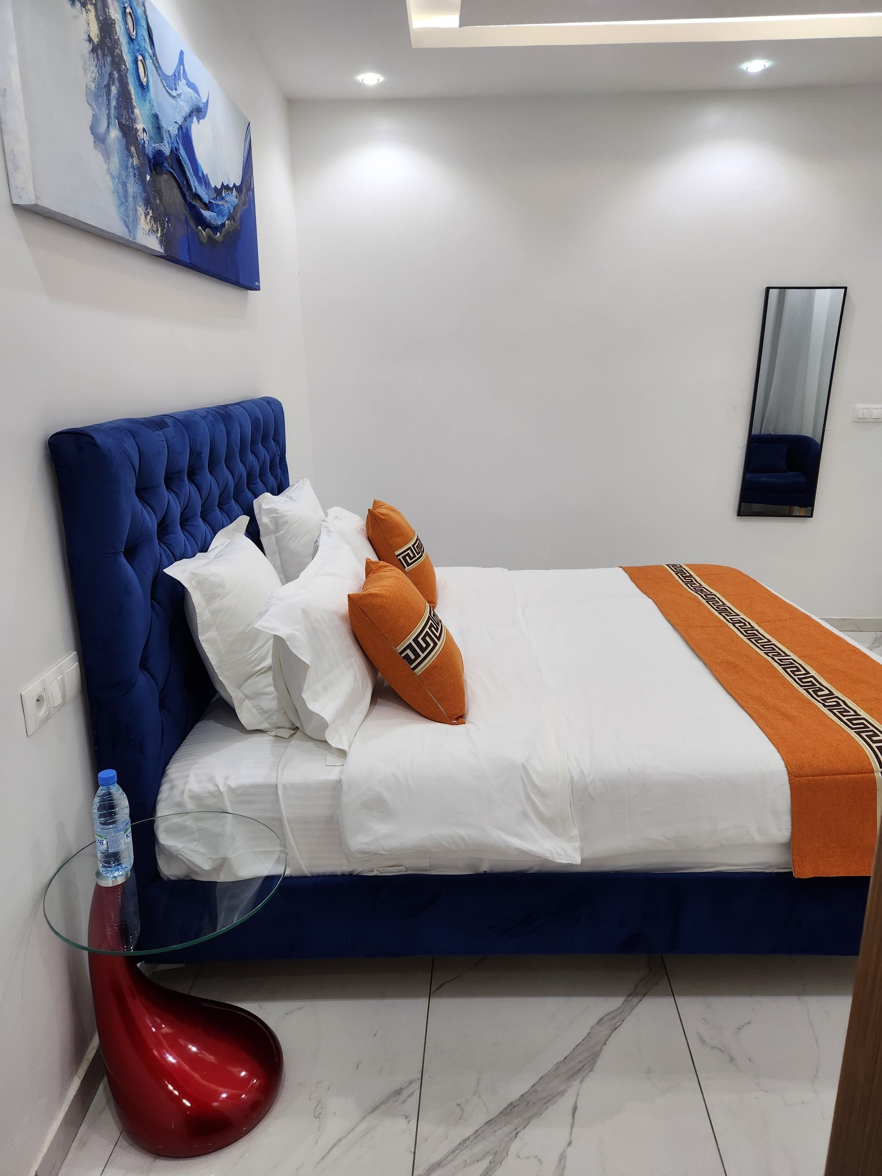 A bedroom with a blue upholstered headboard, white bedding, and orange decorative pillows.