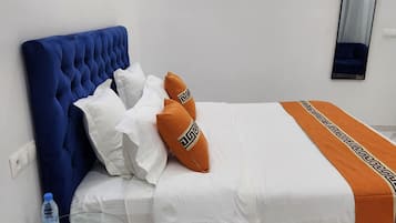 A bedroom with a blue upholstered headboard, white bedding, and orange decorative pillows.