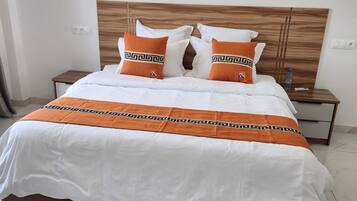 A neatly made bed with white and orange bedding, a wooden headboard, and a marble floor.