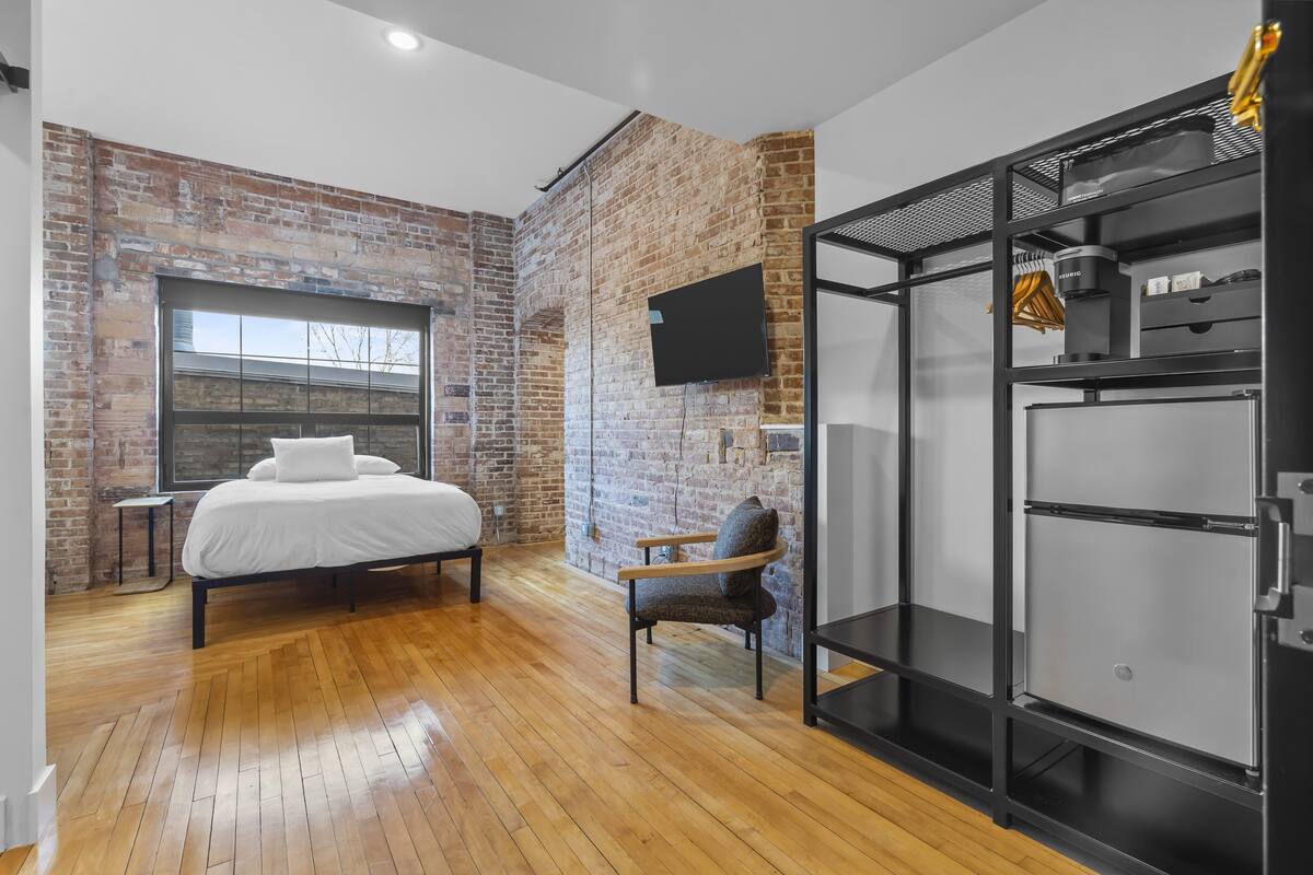 Une chambre moderne avec un mur en briques, un lit, une chaise et un meuble de rangement noir.