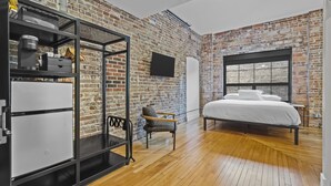 Une chambre avec un mur en briques, un lit, une armoire et un téléviseur.