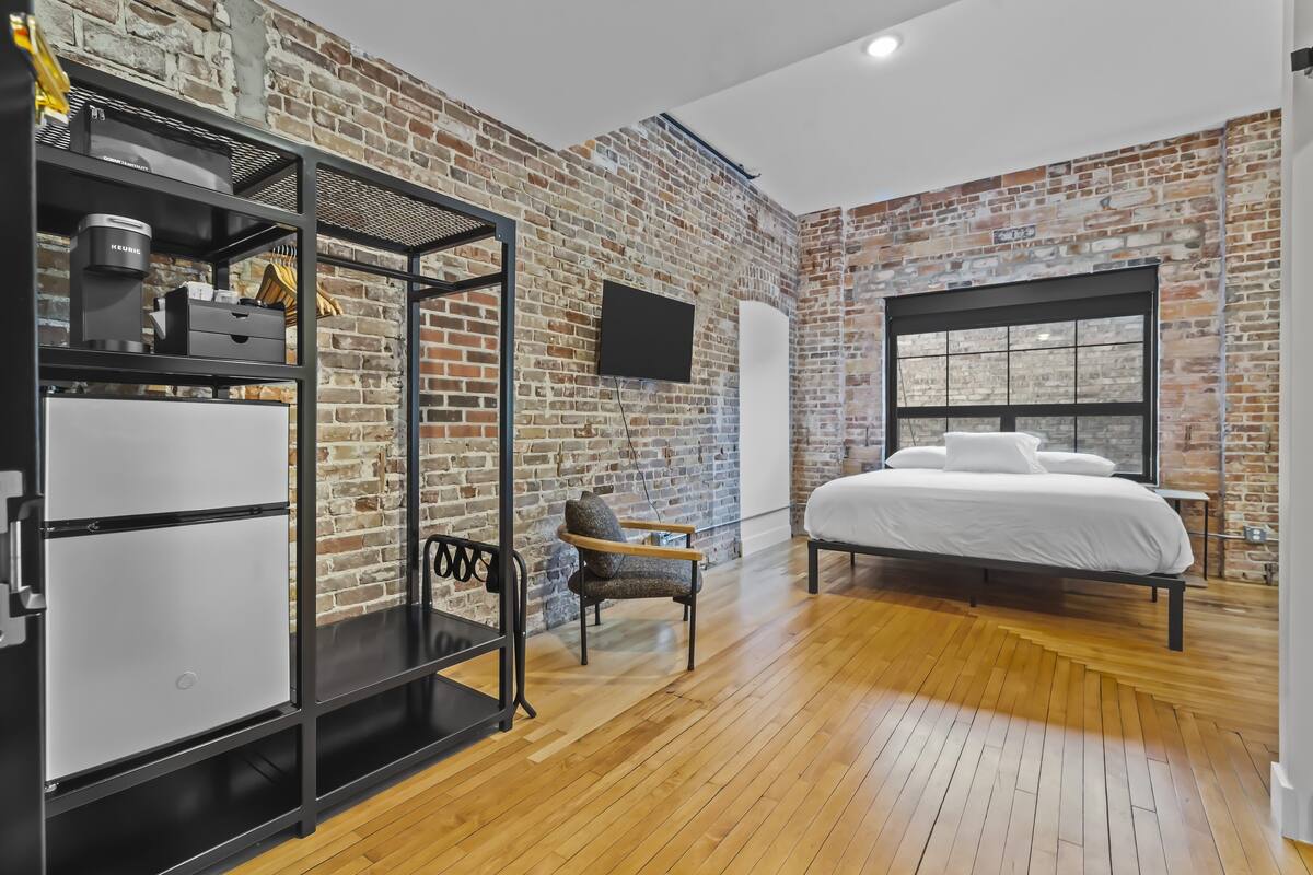 Une chambre avec un mur en briques, un lit, une armoire et un téléviseur.