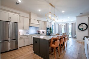 A modern kitchen with stainless steel appliances, a central island with bar stools, and a chandelier.