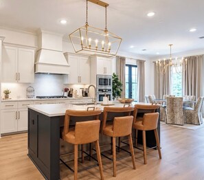 A modern kitchen with a central island, bar seating, and a dining area with a chandelier. - The SLOHouse, Walk to Sq+Campus, VelvetDitchVillas (Oxford)
