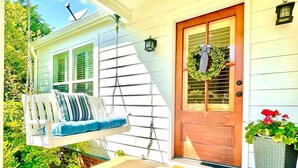 A porch with a swing, a door with a wreath, and a planter with flowers. - The Sivley 2BR Classic Home by Velvet Ditch Villas (Oxford)