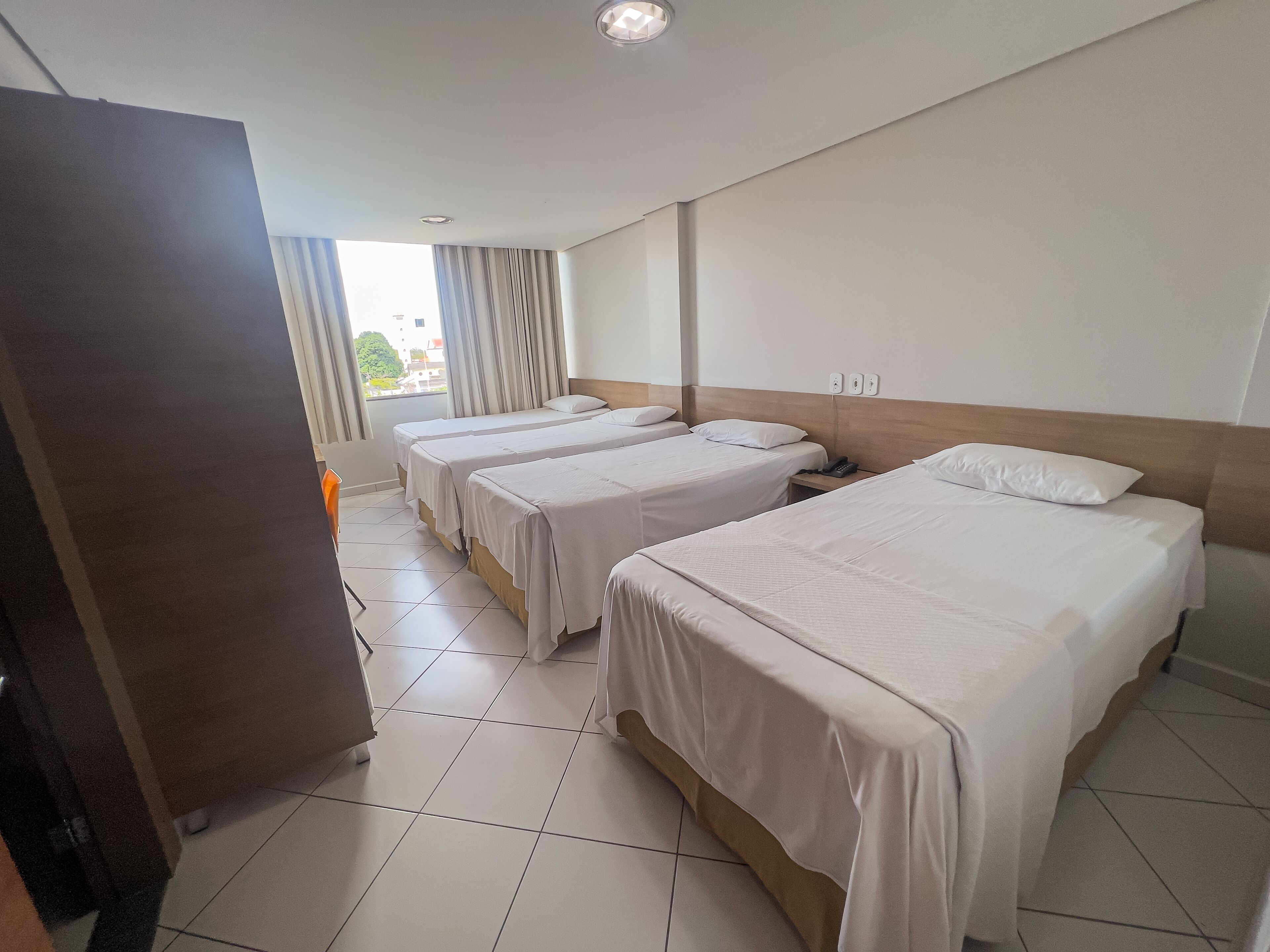 Habitació d'hotel amb tres llits individuals, un panell frontal de fusta, un escriptori i una cadira.