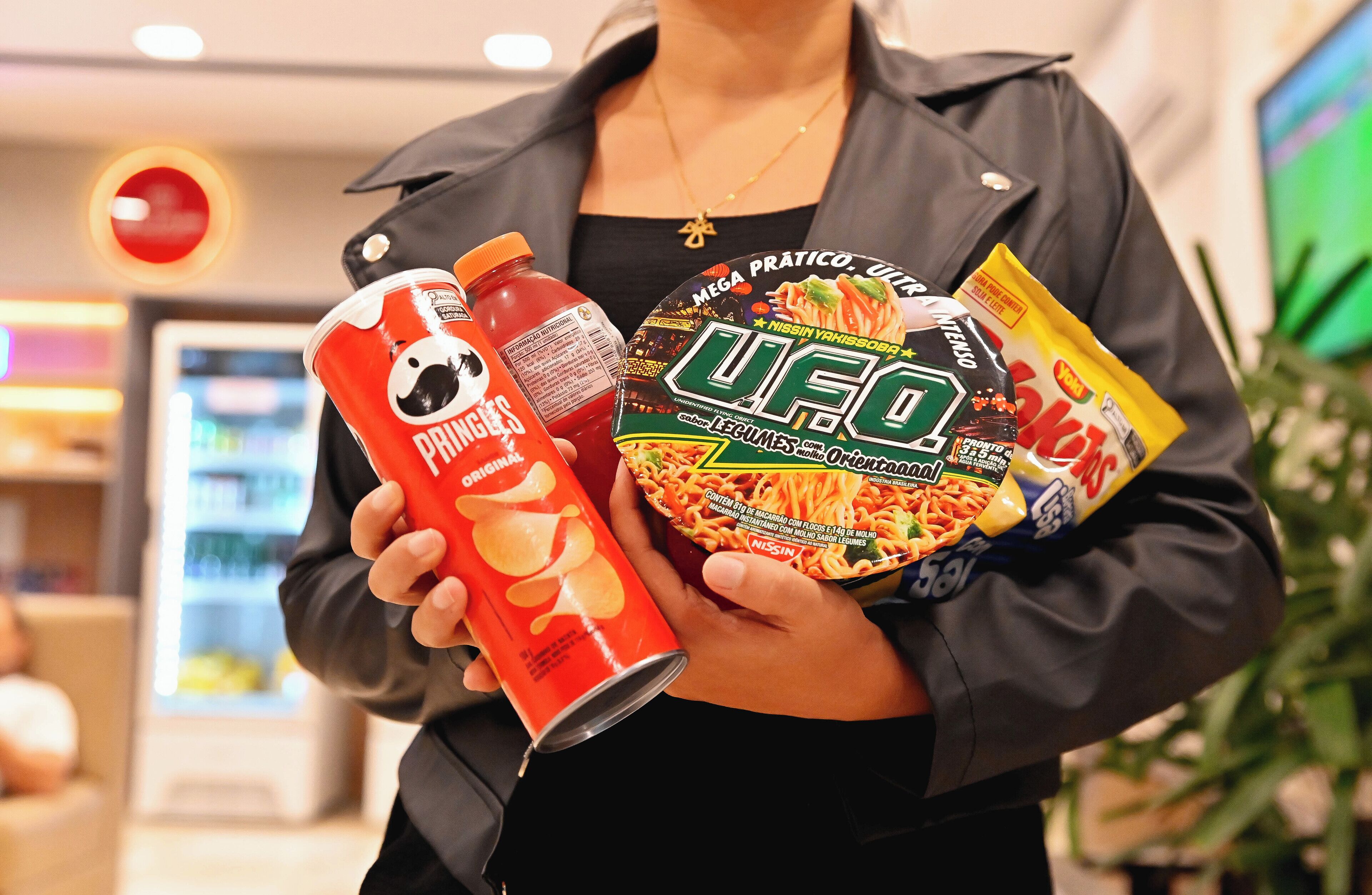 En person som håller i en burk Pringles, en flaska ketchup och ett paket med UFO-nudlar.