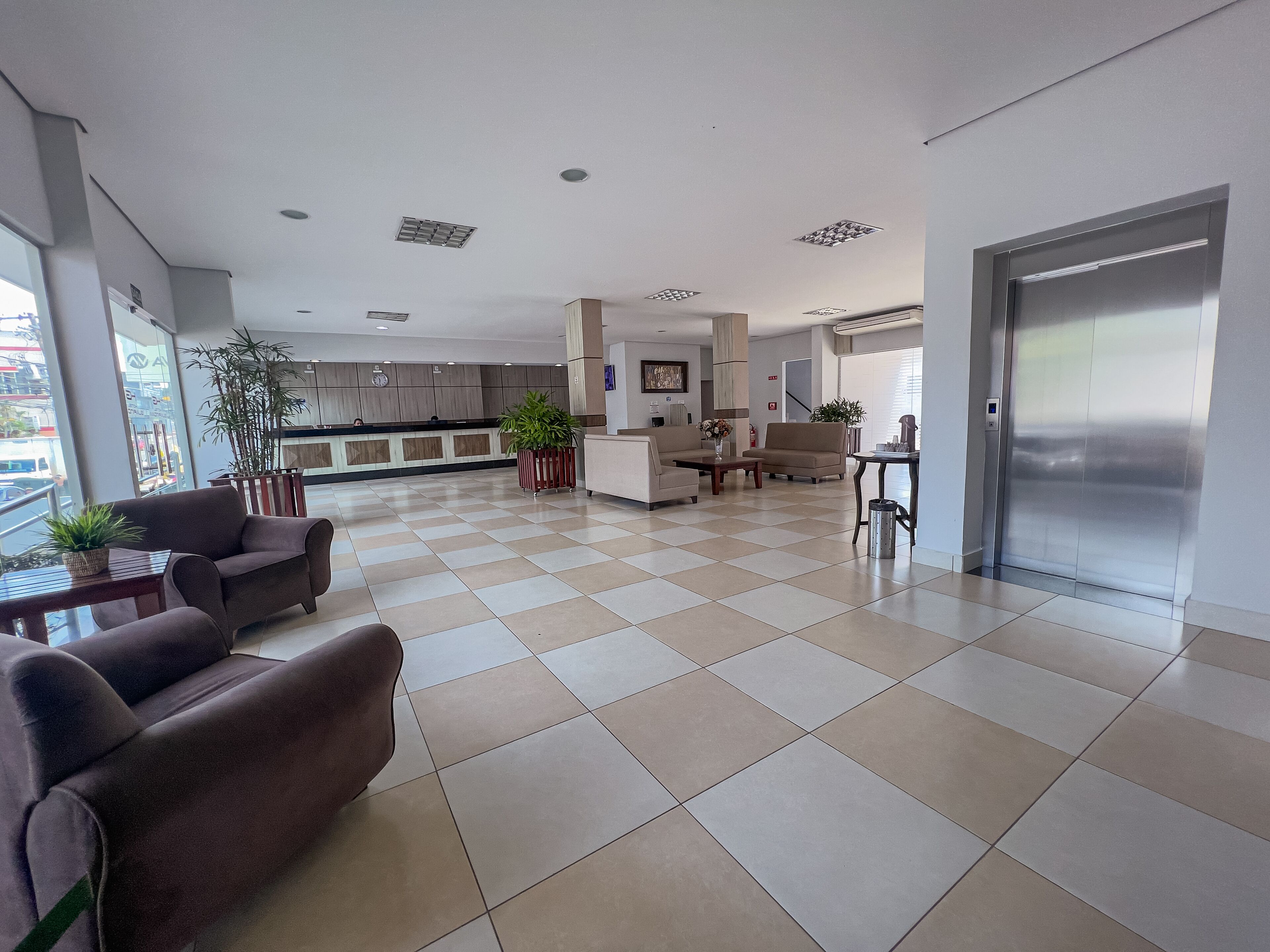 A spacious lobby with a checkered floor, a reception desk, seating area, and a staircase leading to an elevator.