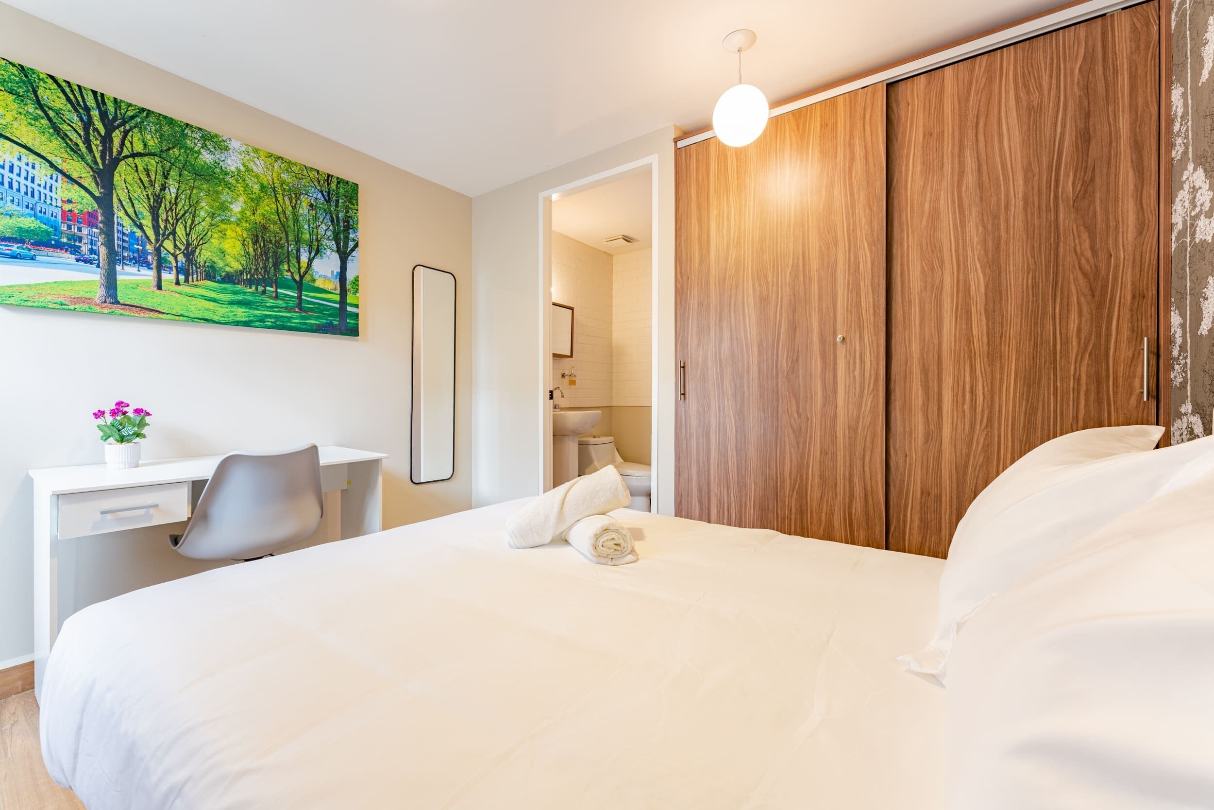 Una camera d'albergo moderna con un letto grande, una scrivania con una sedia, un armadio in legno e un quadro raffigurante un parco.