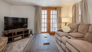 A living room with a flat-screen TV, a sofa, a coffee table, and a sliding glass door to the outside. - 4BD House, Your Central Suburban Oasis, City Lights, Quiet Nights (Wauwatosa)
