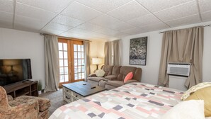 A hotel room with a bed, a sofa, a TV, a lamp, and a window with curtains. - 4BD House, Your Central Suburban Oasis, City Lights, Quiet Nights (Wauwatosa)
