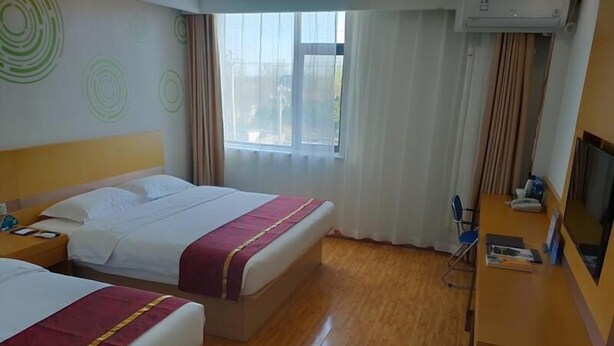 Une chambre d’hôtel avec deux lits, un bureau avec une chaise, une télévision et une fenêtre avec des rideaux.
