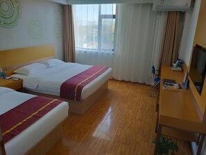 Ein Hotelzimmer mit zwei Betten, einem Schreibtisch mit Stuhl, einem Fernseher und einem Fenster mit Vorhängen.