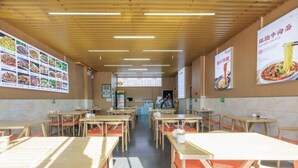 L’intérieur d’un restaurant, avec des tables et des chaises en bois, des panneaux affichant le menu sur les murs et un comptoir au fond de la salle.