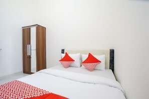 Une chambre à coucher avec un lit, du linge de lit blanc, une armoire en bois et deux oreillers rouges.