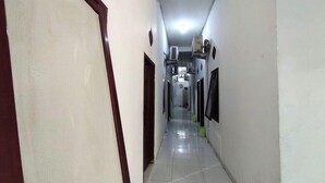Un couloir étroit au sol carrelé, une porte sur la gauche et un climatiseur fixé au mur sur la droite.