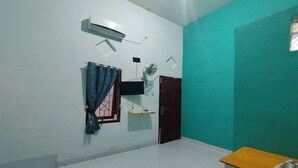Une pièce avec un ventilateur de plafond blanc, un téléviseur fixé au mur, une porte et une petite table.
