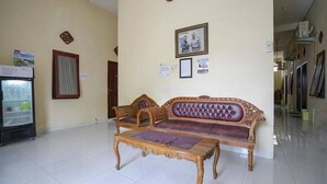 Un hall d’entrée spacieux, avec un canapé en bois et un fauteuil assorti, une petite table, un réfrigérateur et une horloge au mur.
