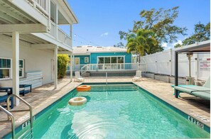 A swimming pool with a 4 FT depth marker, a covered seating area, and a building with a balcony.