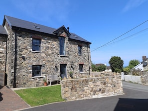 A stone building with a sloped roof, a bench outside, and a stone wall in front. - The Pottery (Newport)
