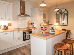 A modern kitchen with white cabinets, a stainless steel range hood, a wooden countertop, and a fruit bowl. - The Pottery (Newport)