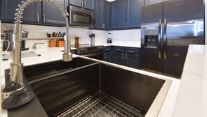 Een moderne keuken met donkerblauwe kastjes, roestvrijstalen apparatuur en een strakke kraan.