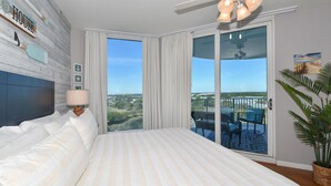 Een slaapkamer met een groot bed, een plafondventilator, uitzicht op de stad en een balkon met stoelen.