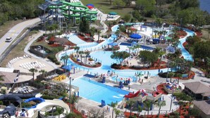 Eine Vogelperspektive eines Wasserparks mit mehreren Rutschen, einem großen Schwimmbecken und der umliegenden Bepflanzung.