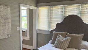 A bedroom with a bed, a window with blinds, a door, and a wall-mounted light fixture. - Cozy Carriage House 2 Blocks from Oxford Square (Oxford)