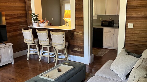 A modern living room with a grey sofa, a small ottoman, and a dining area with wooden chairs and a table. - Cozy Carriage House 2 Blocks from Oxford Square (Oxford)