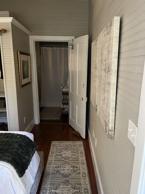 A hallway with a bed, a rug, a door leading to a bathroom, and a wall with a picture frame. - Cozy Carriage House 2 Blocks from Oxford Square (Oxford)