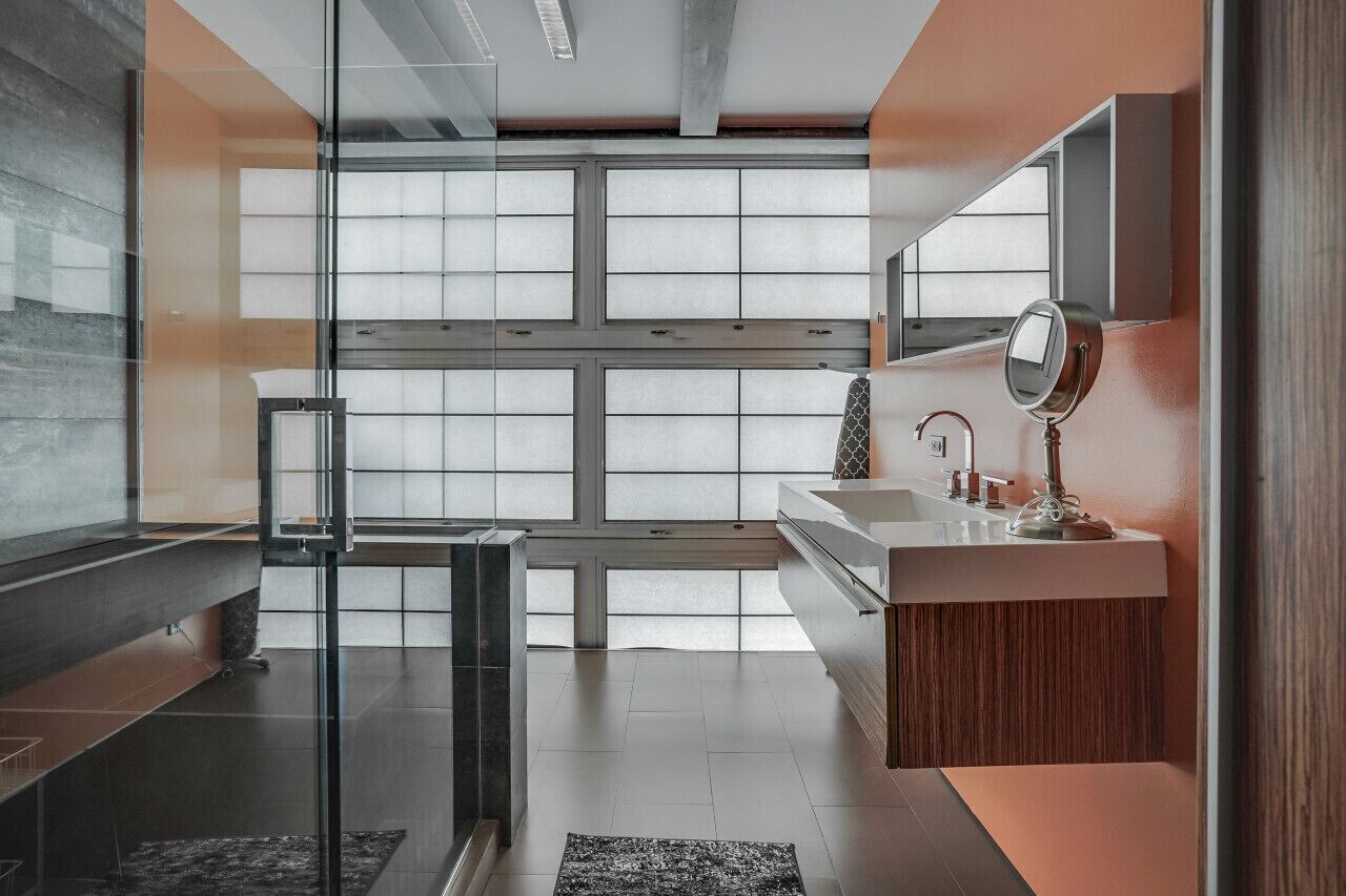 Un baño moderno con separador de vidrio, un espejo grande y un mueble de tocador de madera.