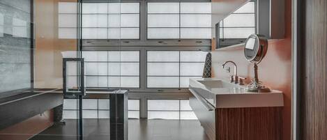Un baño moderno con separador de vidrio, un espejo grande y un mueble de tocador de madera.