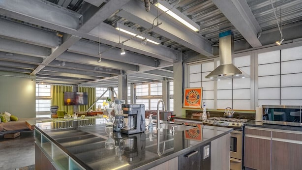 Une cuisine spacieuse dotée d’un grand îlot central, d’appareils électroménagers en acier inoxydable et d’un plafond haut avec des poutres apparentes.