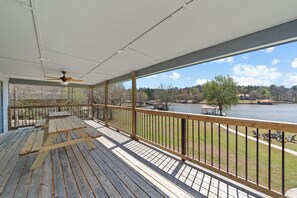 A wooden deck with a picnic table and a ceiling fan, overlooking a lake with boats and a dock. - Sunset Estate 7 bedrooms, Sleeps 18! + Game Room (Sparta)