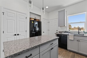 Una cocina moderna con encimeras de granito, armarios blancos y lavavajillas negro.