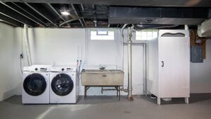 Una sala de bugaderia amb dues rentadores, una bassina gran i un armari blanc.