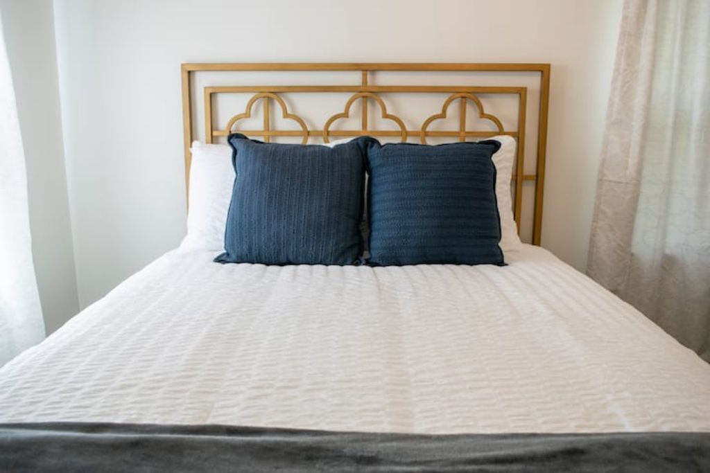 A bed with a wooden headboard, white bedding, and two dark blue pillows.