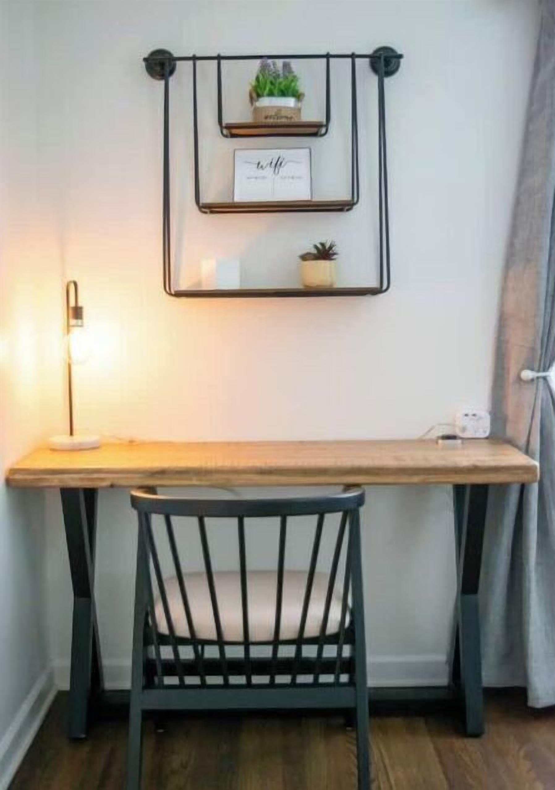 Un escritorio de madera con una silla negra, una estantería de pared con plantas y un espejo de pared.