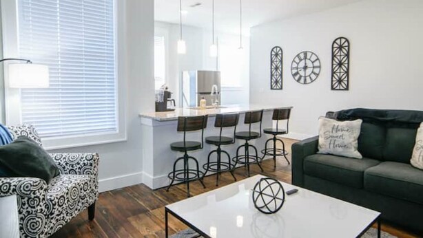 A modern living room with a sofa, a coffee table, and a dining area with bar stools.